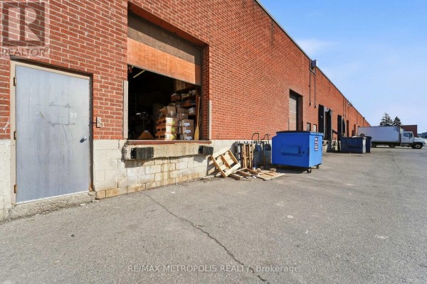 Loading dock with open bay door, pallets, and industrial bins next to a brick building. - 35 - 120 Dynamic Drive, Toronto