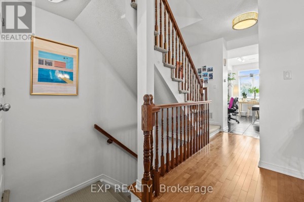 Hallway with light wood floors, a carpeted staircase with oak railings, and artwork on the wall. - 35 - 957 Cummings Avenue, Ottawa
