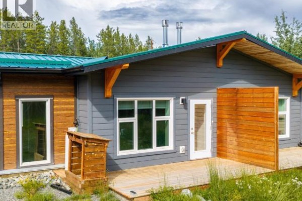 Side exterior view of a grey duplex with a green metal roof and wooden deck. - 35- Takhini Meadows Drive, Whitehorse North