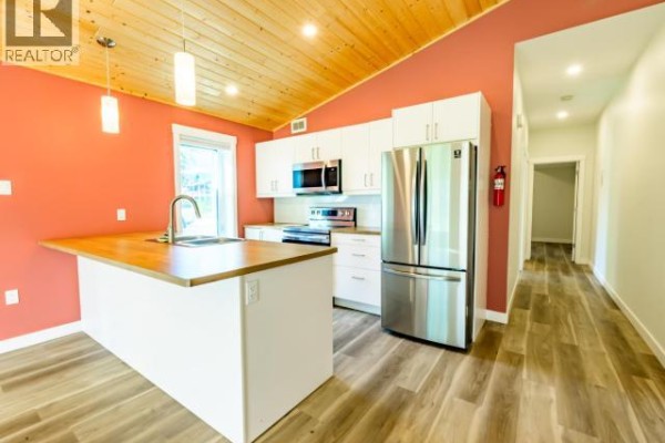 Kitchen with white cabinets, stainless steel appliances, coral walls, and wood plank flooring. - 35- Takhini Meadows Drive, Whitehorse North