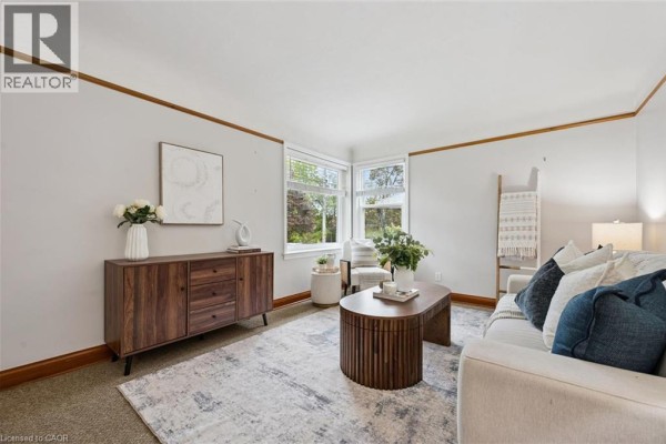 Living room with sofa, wooden furniture, and windows showing green trees outside. - 35 Acacia Street, Kitchener
