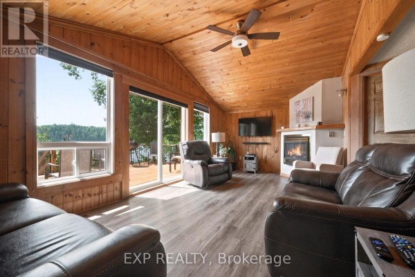 Living room with leather couches, fireplace, large windows, and wood-paneled walls and ceiling. - 35 Downing Lane, Greater Madawaska