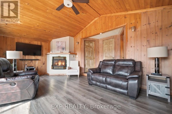Living room with leather couches, fireplace, wood-paneled walls and ceiling, and wood doors. - 35 Downing Lane, Greater Madawaska