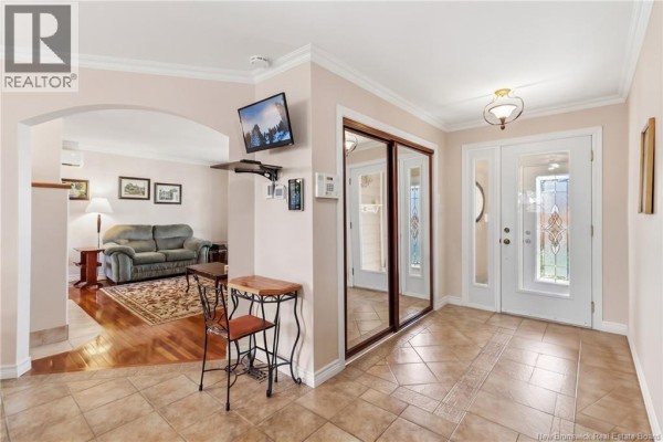 Interior front entryway with beige tile flooring, mirrored closet doors, and a wooden staircase. - 35 Firwood Crescent, Moncton