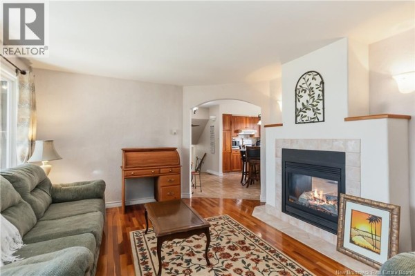 Living room with two sofas, a rug, a wooden roll-top desk, and a sunroom view. - 35 Firwood Crescent, Moncton