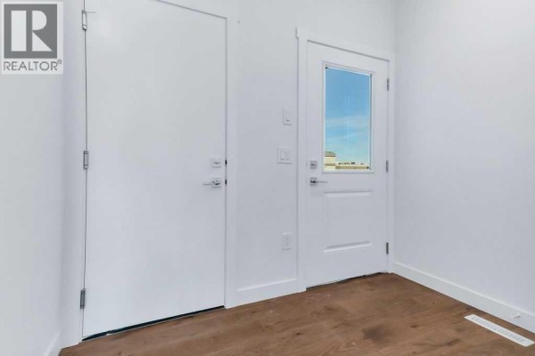 Interior view of a hallway with two white doors, one with a glass panel, and wooden floors. - 35 Linden Place, Rural Red Deer County