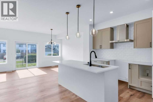 Modern kitchen with a white island, beige cabinets, white subway tile backsplash, and pendant lights. - 35 Linden Place, Rural Red Deer County