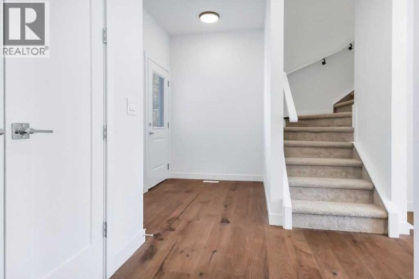 Interior view of a home entrance with hardwood floors, white walls, and a carpeted staircase. - 35 Linden Place, Rural Red Deer County
