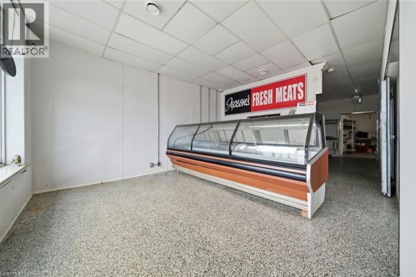 Empty commercial interior showing a refrigerated display case, white walls, and speckled floor. - 35 Main Street N, Hagersville