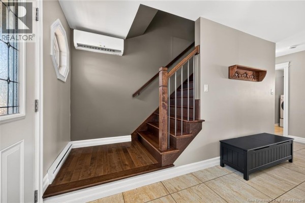 Interior view of a home entrance with a wooden staircase and a black storage bench. - 35 Ruby Way, Moncton
