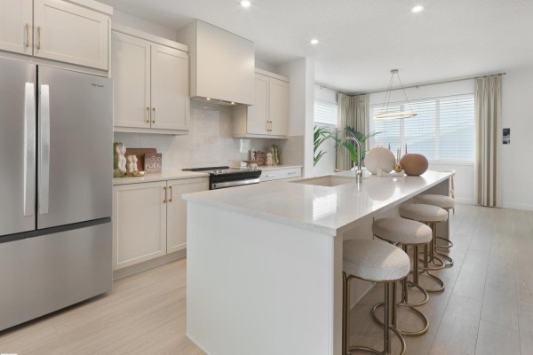 A stainless steel refrigerator is on the left side of the kitchen, with a large island and dining area. - 350 Stiles Wy, Leduc