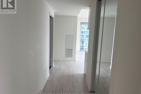 Hallway with light wood-look flooring and white walls, leading to a living area. - 3502 - 5 Buttermill Avenue, Vaughan