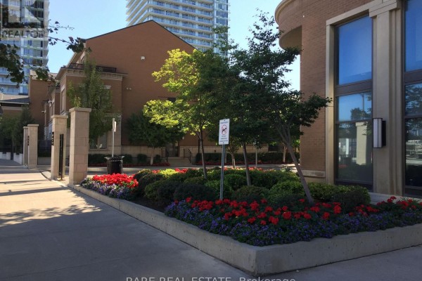 Landscaped garden with red and purple flowers, bushes, and trees outside a brick building. - 3505 - 385 Prince Of Wales Drive, Mississauga