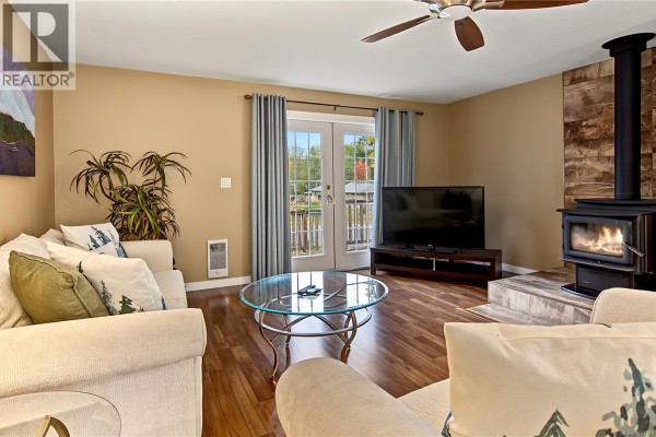 Living room with a wood-burning stove, television, sofa, and glass coffee table. - 3505 Harris Cres, Qualicum Beach