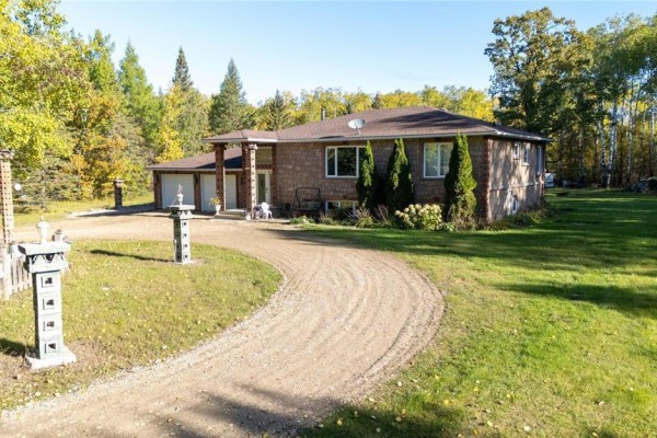 Front view of a tan-sided house with a circular driveway and trees. - 35091 Gueret 44e Road, La Broquerie