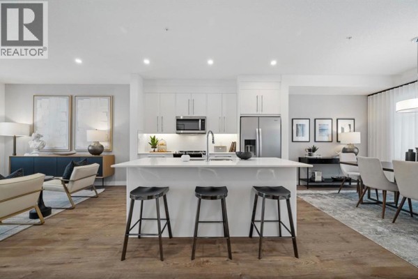Open-concept kitchen and living area with white cabinets, quartz island with bar stools, and stainless steel appliances. - 351, 141 Prince Court, Rural Rocky View County