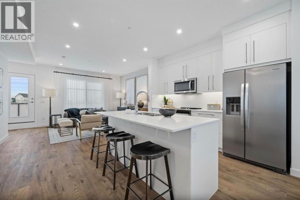 Modern kitchen with white island, stainless steel appliances, and adjacent living room with neutral furnishings. - 351, 141 Prince Court, Rural Rocky View County