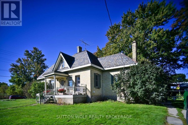 Side view of the yellow brick house showing the peaked roof, chimney, and covered porch. - 351 Albert Street, Strathroy Caradoc