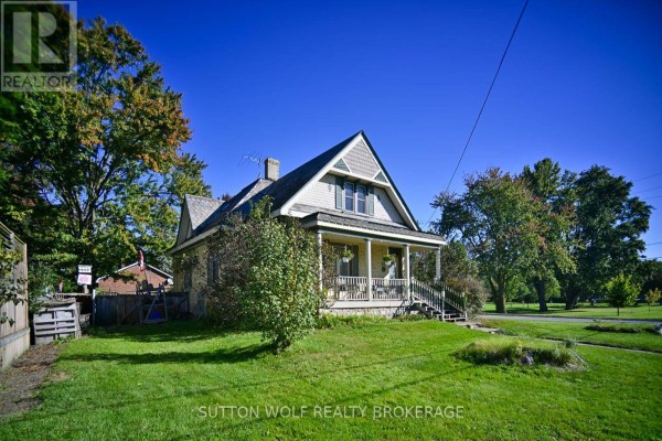 Side view of the yellow brick house with a covered porch and mature trees in the yard. - 351 Albert Street, Strathroy Caradoc