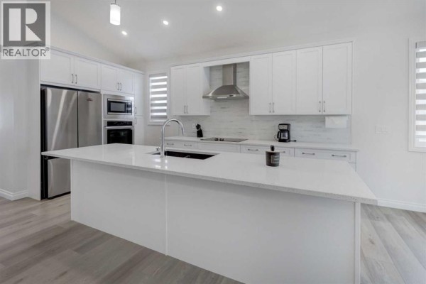 White kitchen with a large island, stainless steel appliances, and quartz countertops. - 351 Baywater Common Sw, Airdrie