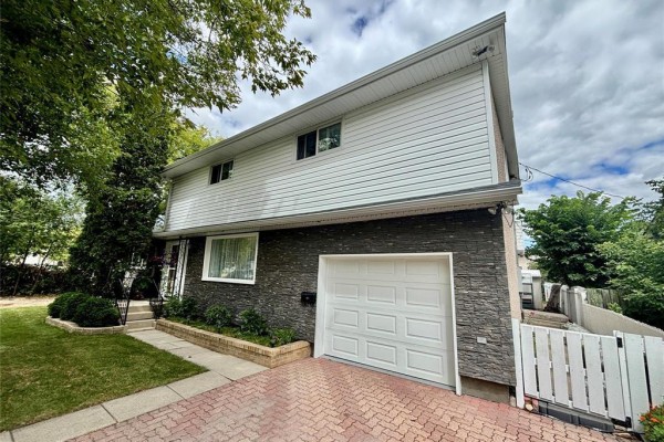 View of the house facade with a white garage door, stone exterior, and a paved driveway. - 351 Queen Avenue, Selkirk