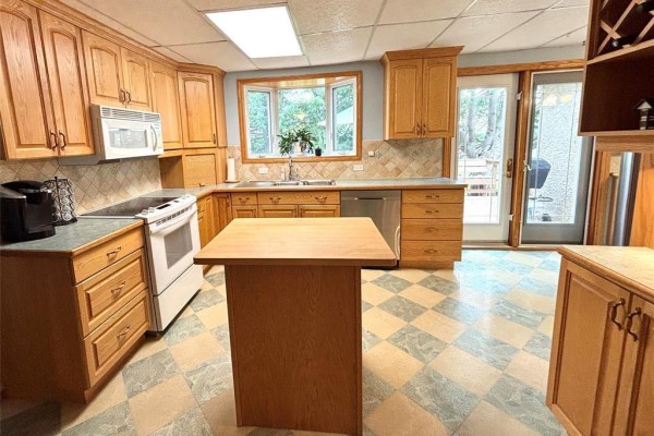 Kitchen with light oak cabinets, white appliances, bay window, and a checkered linoleum floor. - 351 Queen Avenue, Selkirk