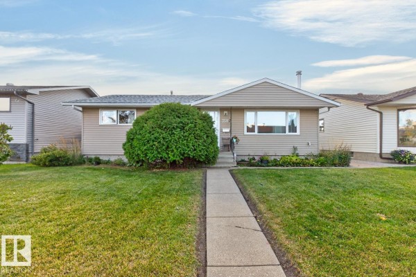 Front exterior view of a beige vinyl-sided bungalow with a neatly trimmed front lawn and walkway. - 3511 106 Av Nw, Edmonton