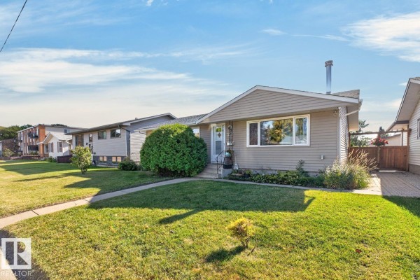 Side view of the beige bungalow with a well-maintained lawn, sidewalk, and neighboring properties. - 3511 106 Av Nw, Edmonton