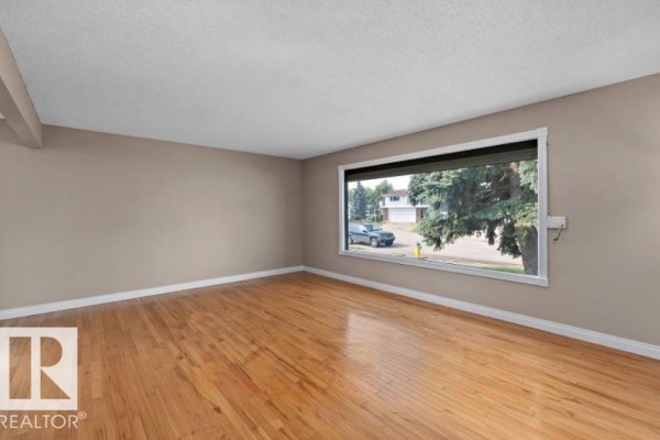 Living room with a large picture window, hardwood floors, and traditional furniture. - 3511 73 St Nw, Edmonton