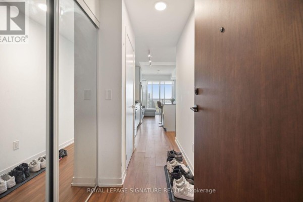 Apartment entryway with a large mirrored closet, wood floors, and shoe racks. - 3512 - 4065 Confederation Parkway, Mississauga