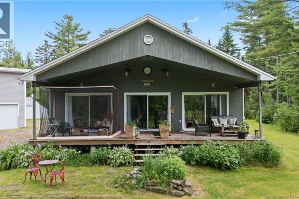 Front facade of a grey house with a covered porch featuring seating areas and sliding glass doors. - 3515 Route 530, Grande Digue