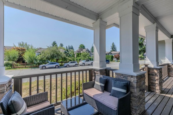 Covered front porch with wicker furniture and stone accents, overlooking a suburban street. - 35159 Mcewen Avenue, Mission