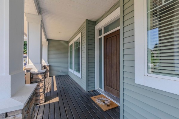 Wooden front door on a covered porch with grey siding and white trim. - 35159 Mcewen Avenue, Mission