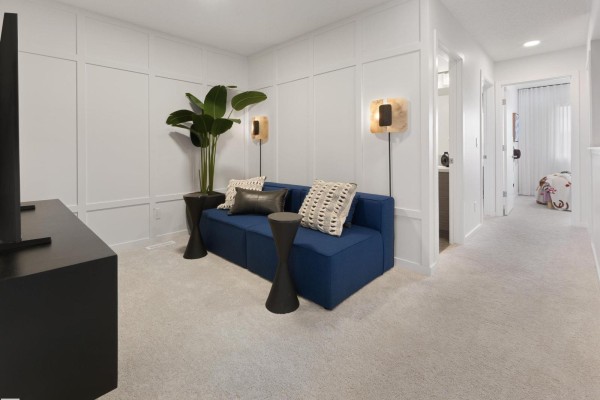 Upstairs hallway and lounge area with a blue sofa, white wall paneling, and carpet. - 352 Stiles Wy, Leduc