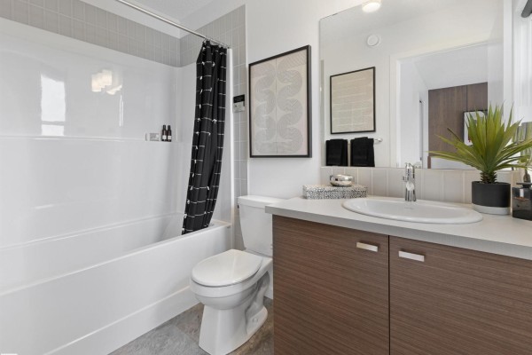 Bathroom with a white bathtub, toilet, wood vanity, and patterned black shower curtain. - 352 Stiles Wy, Leduc