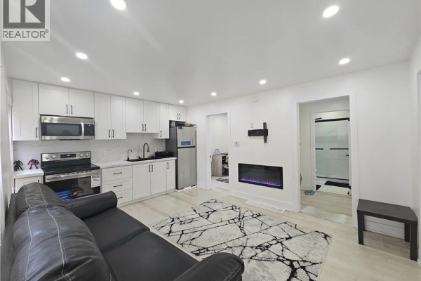 Open concept living area and kitchen with white cabinets, stainless steel appliances, and a modern fireplace. - 352 Weir Street N, Hamilton