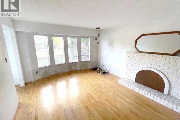 Living room with hardwood floors, bay windows, white brick fireplace, and unfinished walls. - 3520 Broadway Street, Richmond