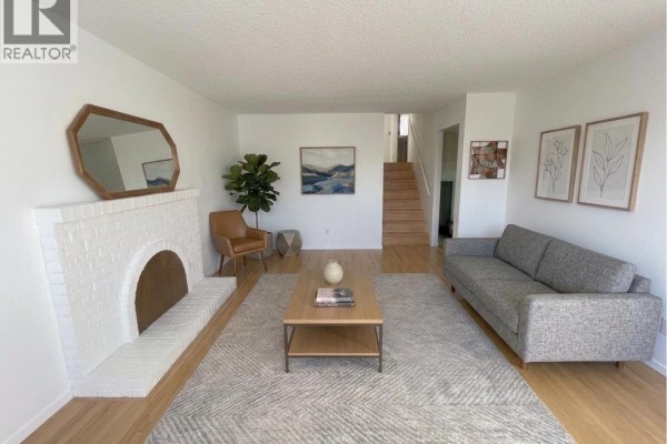 Living room with sofas, armchair, coffee table, rug, fireplace, and stairs to an upper level. - 3520 Broadway Street, Richmond