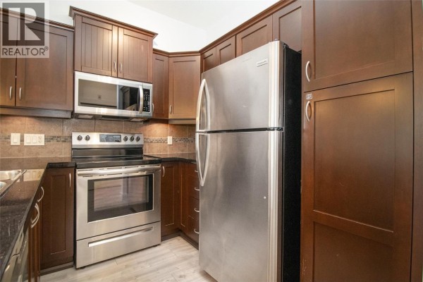 Stainless steel refrigerator and dark wood cabinets in the kitchen. - 3521 Carrington Road Unit# 311, West Kelowna