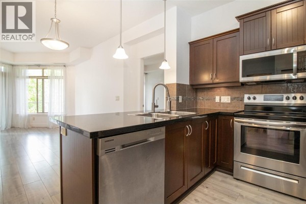 Kitchen island with sink, stainless steel appliances, and view of living area. - 3521 Carrington Road Unit# 311, West Kelowna