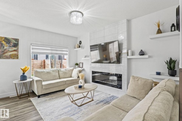 Living room with white walls, tile fireplace, modern furniture, and a large window overlooking the backyard. - 3523 5a Av Sw, Edmonton