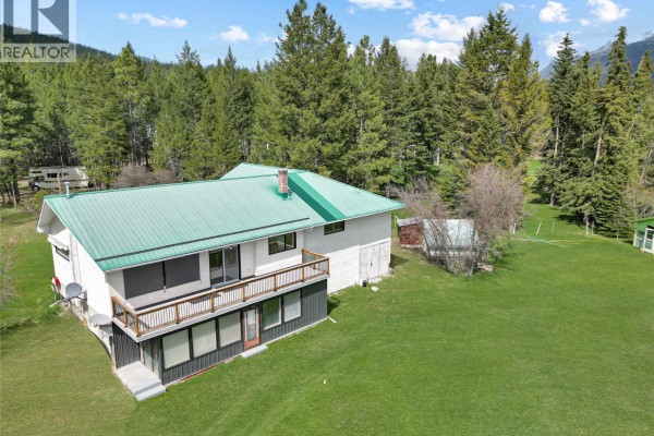 Rear exterior of a house with a large deck, green metal roof, and surrounding trees. - 3526 Island Pond Road, Skookumchuck