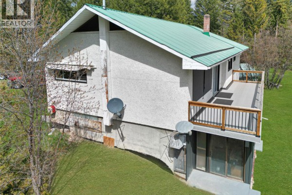 Close-up view of the house exterior showing a deck, stucco walls, and satellite dishes. - 3526 Island Pond Road, Skookumchuck