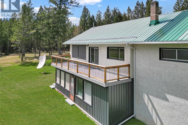 Rear view of the house highlighting the deck, green roof, and wooded landscape. - 3526 Island Pond Road, Skookumchuck
