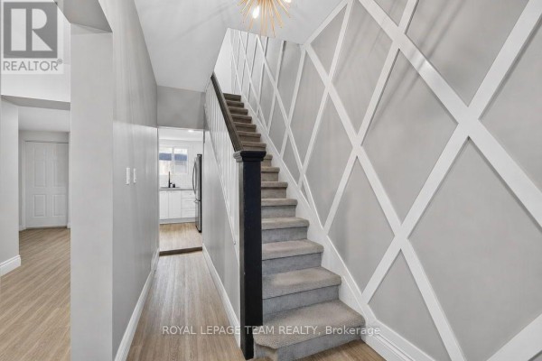 Hallway with grey walls, white lattice design, carpeted stairs with dark wood banister, and view of kitchen. - 353 Arlington Avenue, Ottawa