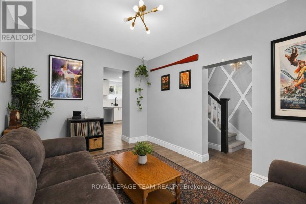 Living room with grey walls, brown sectional sofa, coffee table, rug, and view into kitchen and stairs. - 353 Arlington Avenue, Ottawa