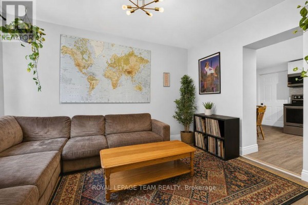 Living room with large world map on wall, brown sectional sofa, coffee table, and view into kitchen. - 353 Arlington Avenue, Ottawa
