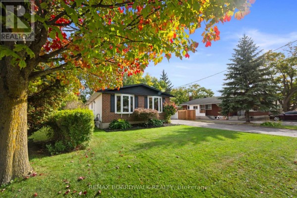 Side exterior view of a brick bungalow with trees showing autumn foliage and a paved driveway. - 353 Churchill Road E, Prescott