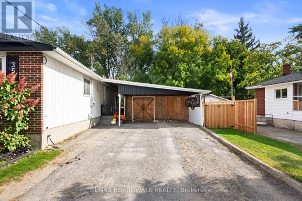 Carport with wooden doors and storage area next to a paved driveway, with a wooden fence. - 353 Churchill Road E, Prescott