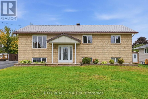 Front exterior of a light beige brick bungalow with a metal roof, white trim, and manicured lawn. - 353 Nelson Street E, Hawkesbury